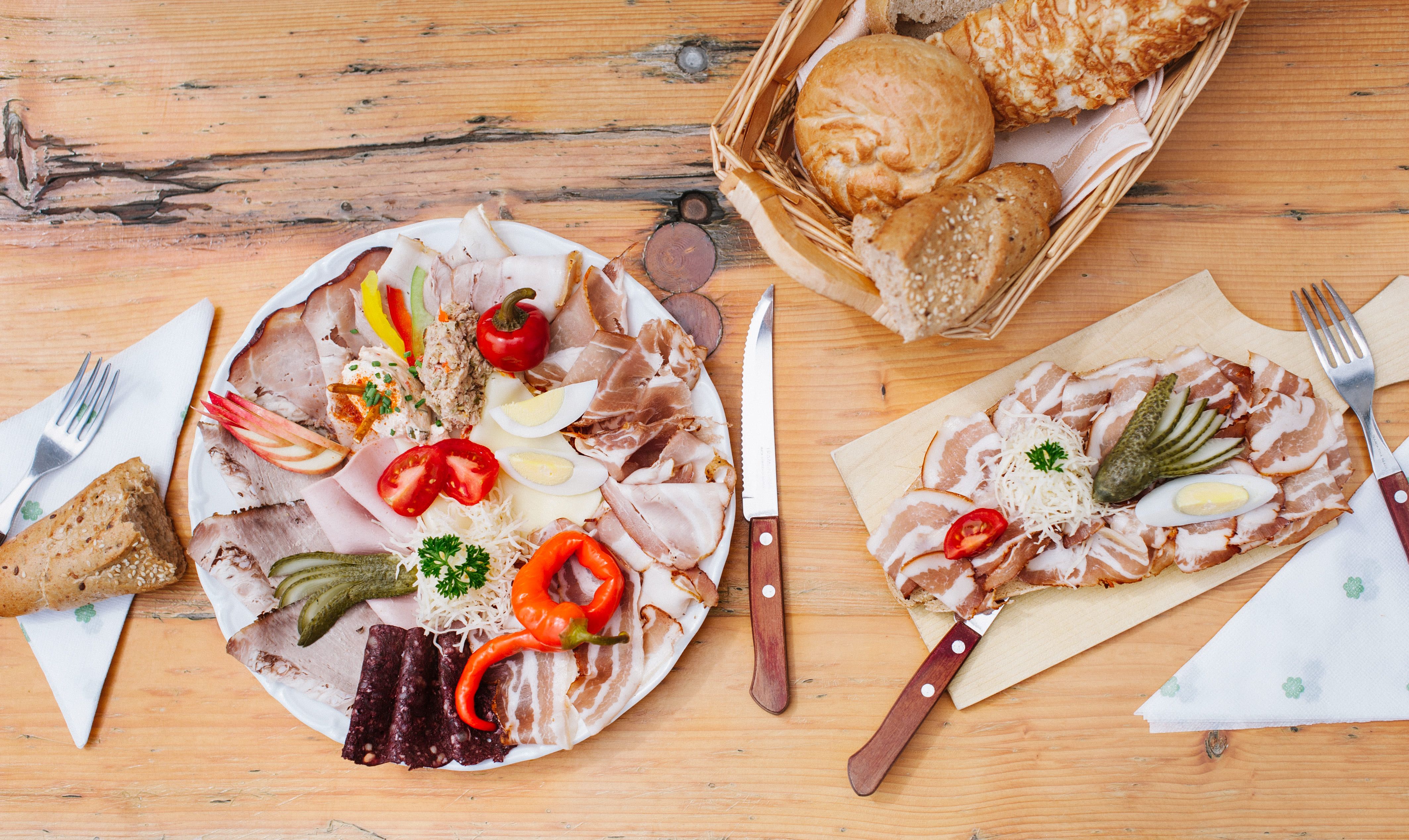 Doska s údeninami, zeleninou a chlebom na drevenom stole.