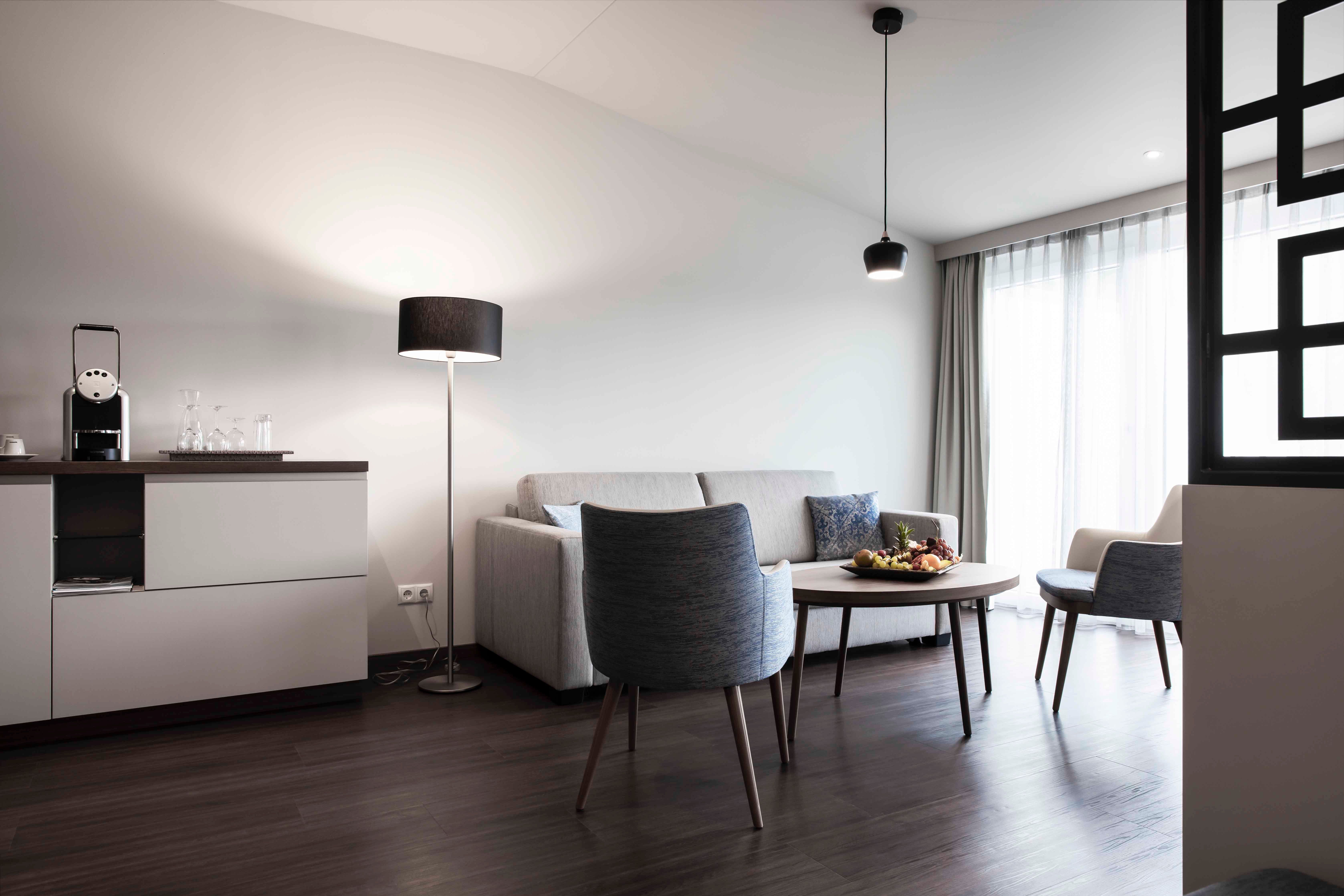 Moderný priestor na sedenie s pohovkou, kreslom, stolom a stojacou lampou vo svetlej miestnosti.