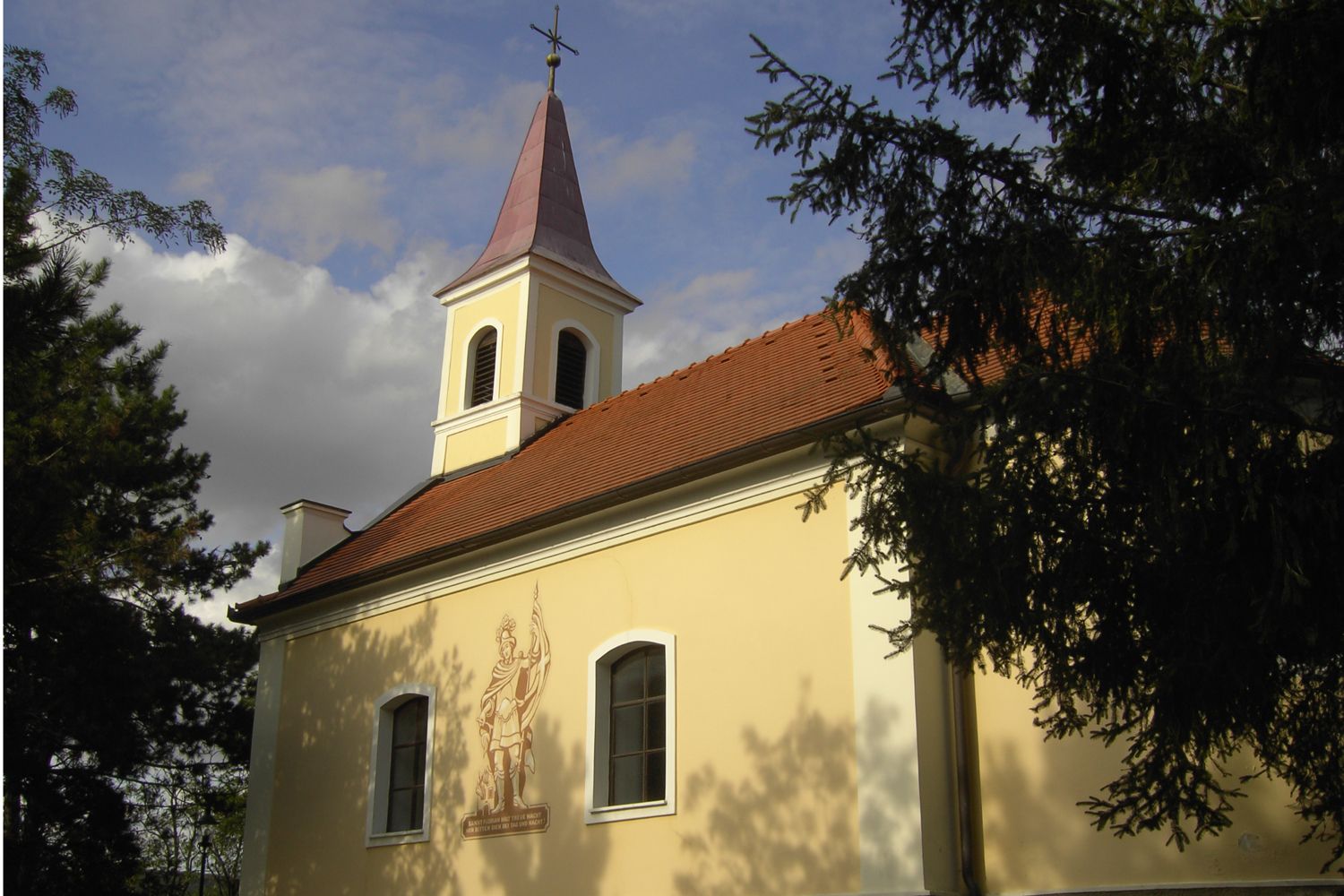 Florianiho kaplnka Oberrohrbach s vežou a nástennou maľbou, obklopená stromami.