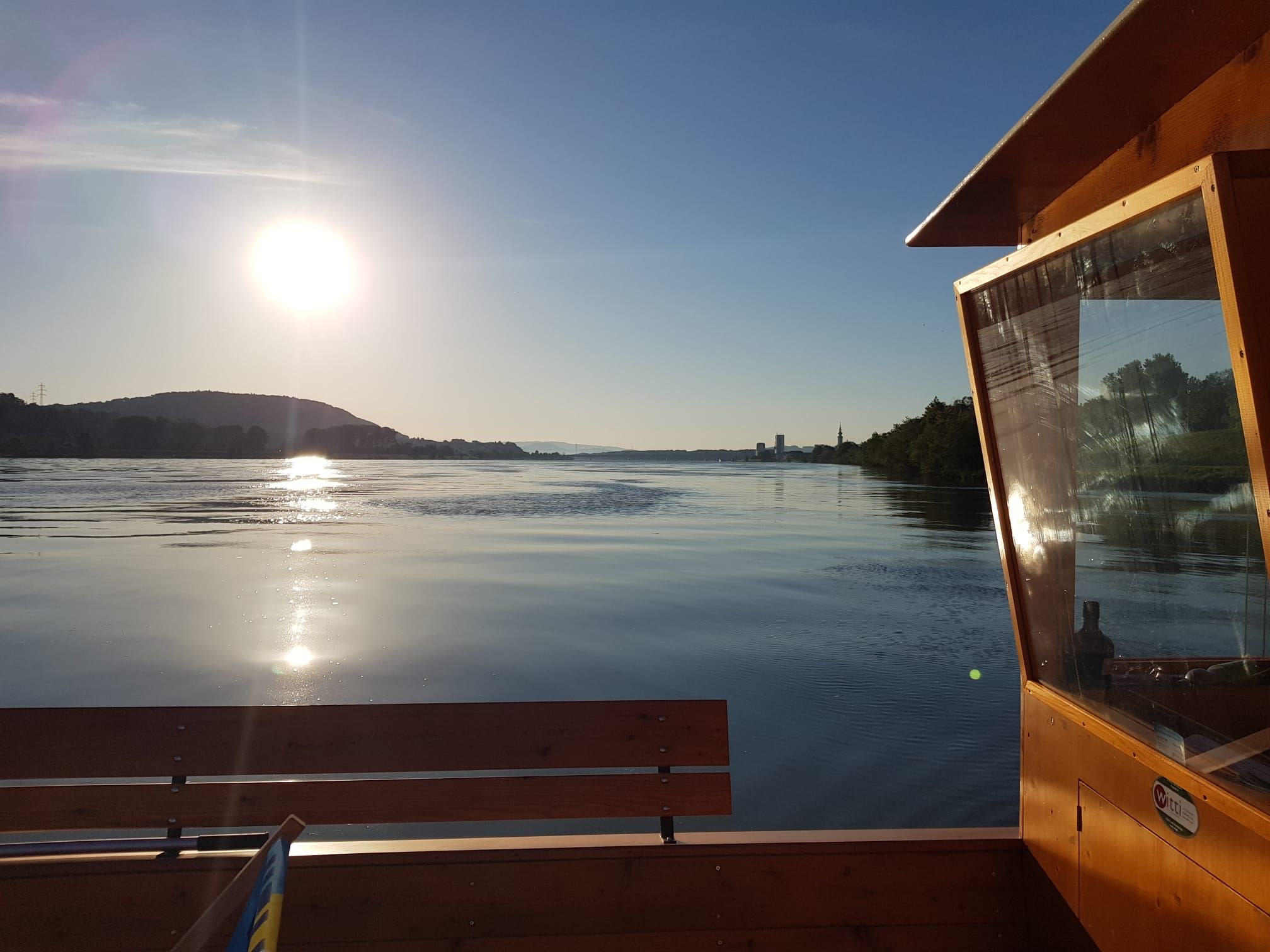 Západ slnka nad pokojnou riekou s drevenou loďou v popredí.
