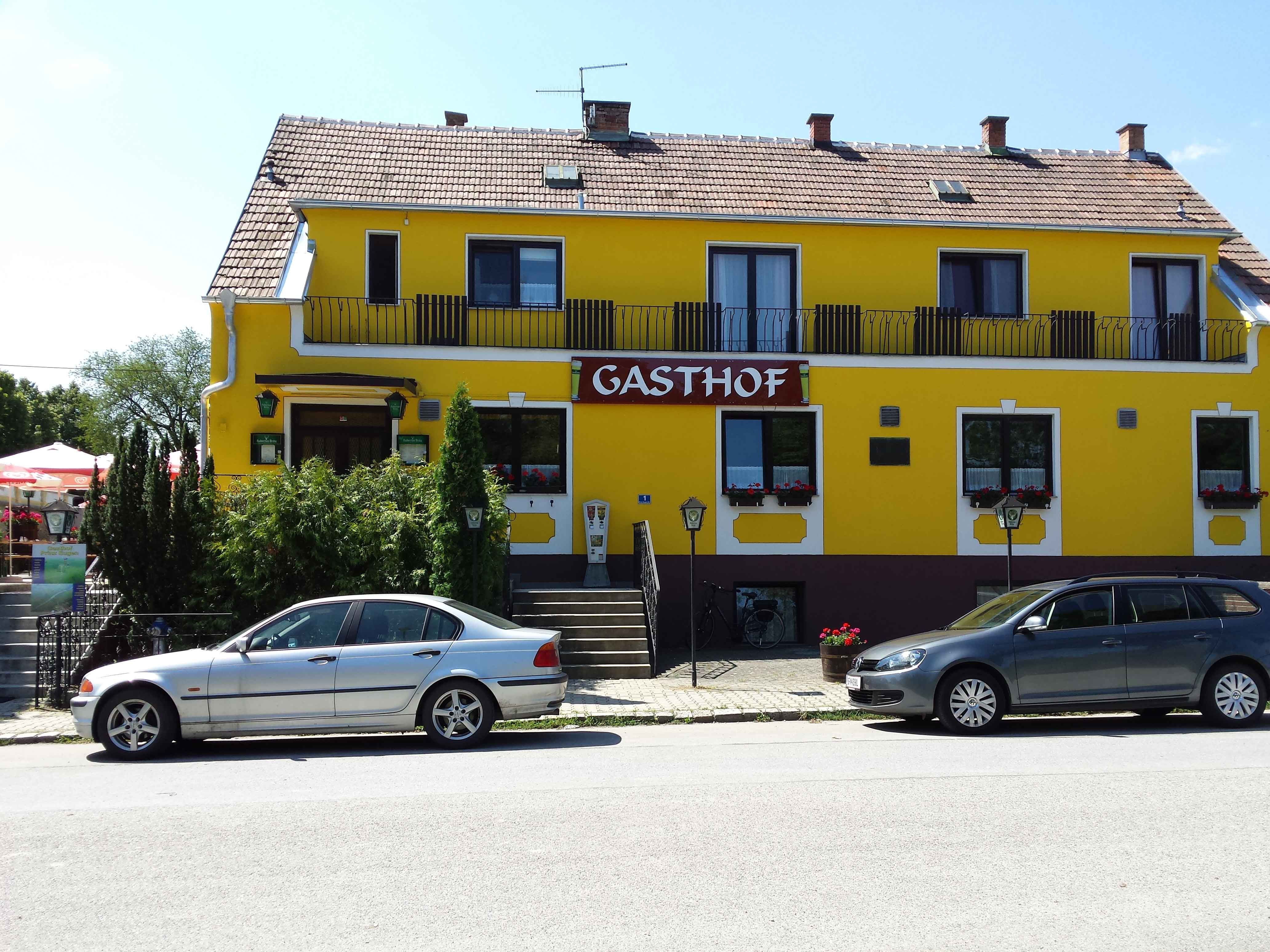 Žltá budova s nápisom "Gasthof", pred ňou zaparkované dve autá.