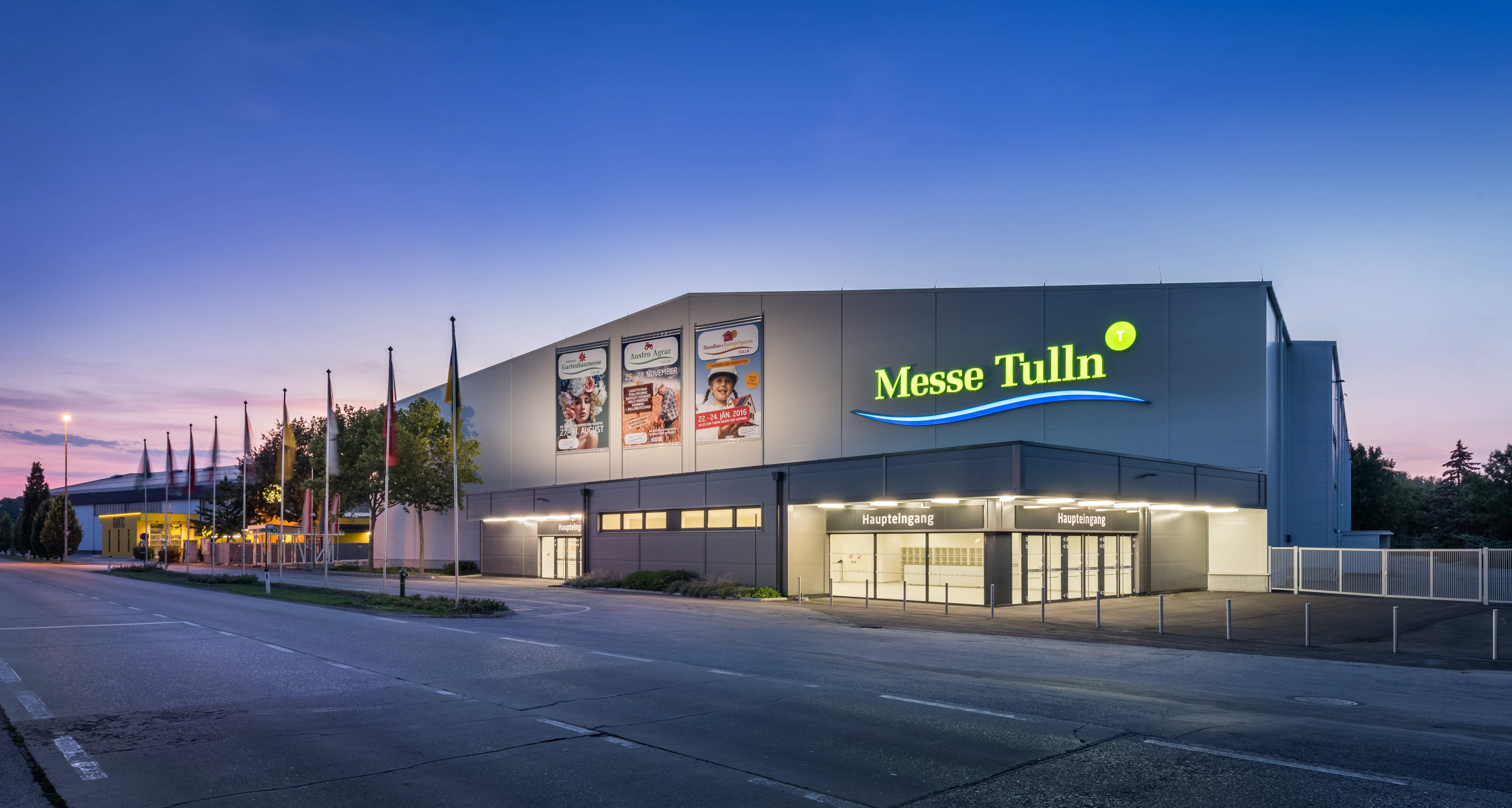 Exteriérový pohľad na výstavisko Tulln za súmraku s osvetleným vchodom a vlajkami.