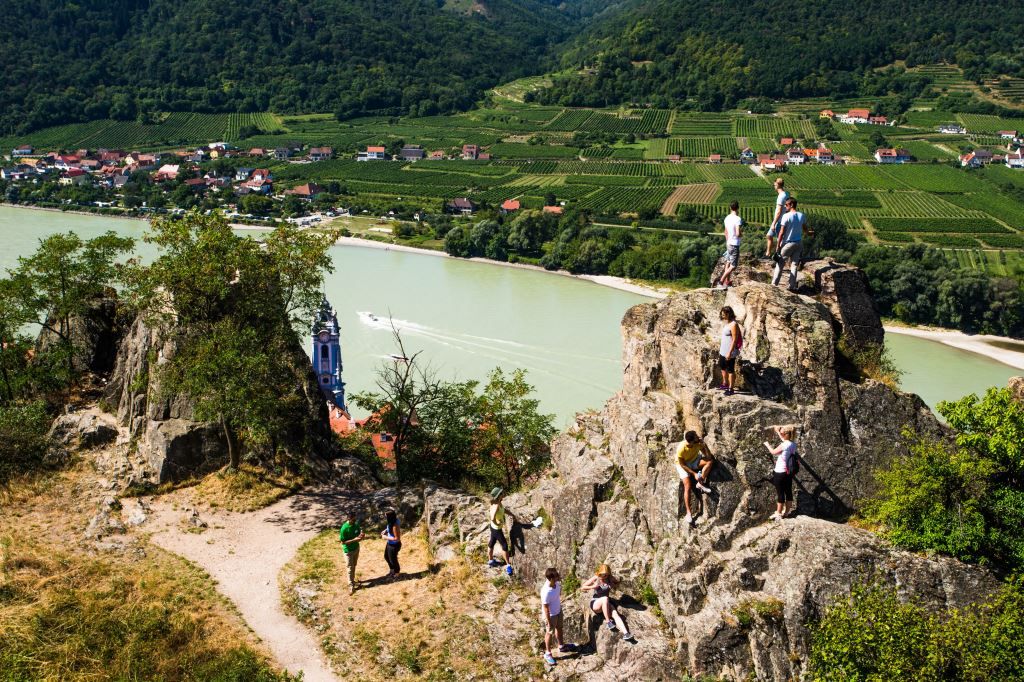 Ľudia lezúci po skalách s výhľadom na Dunaj a vinice v Dürnsteine.
