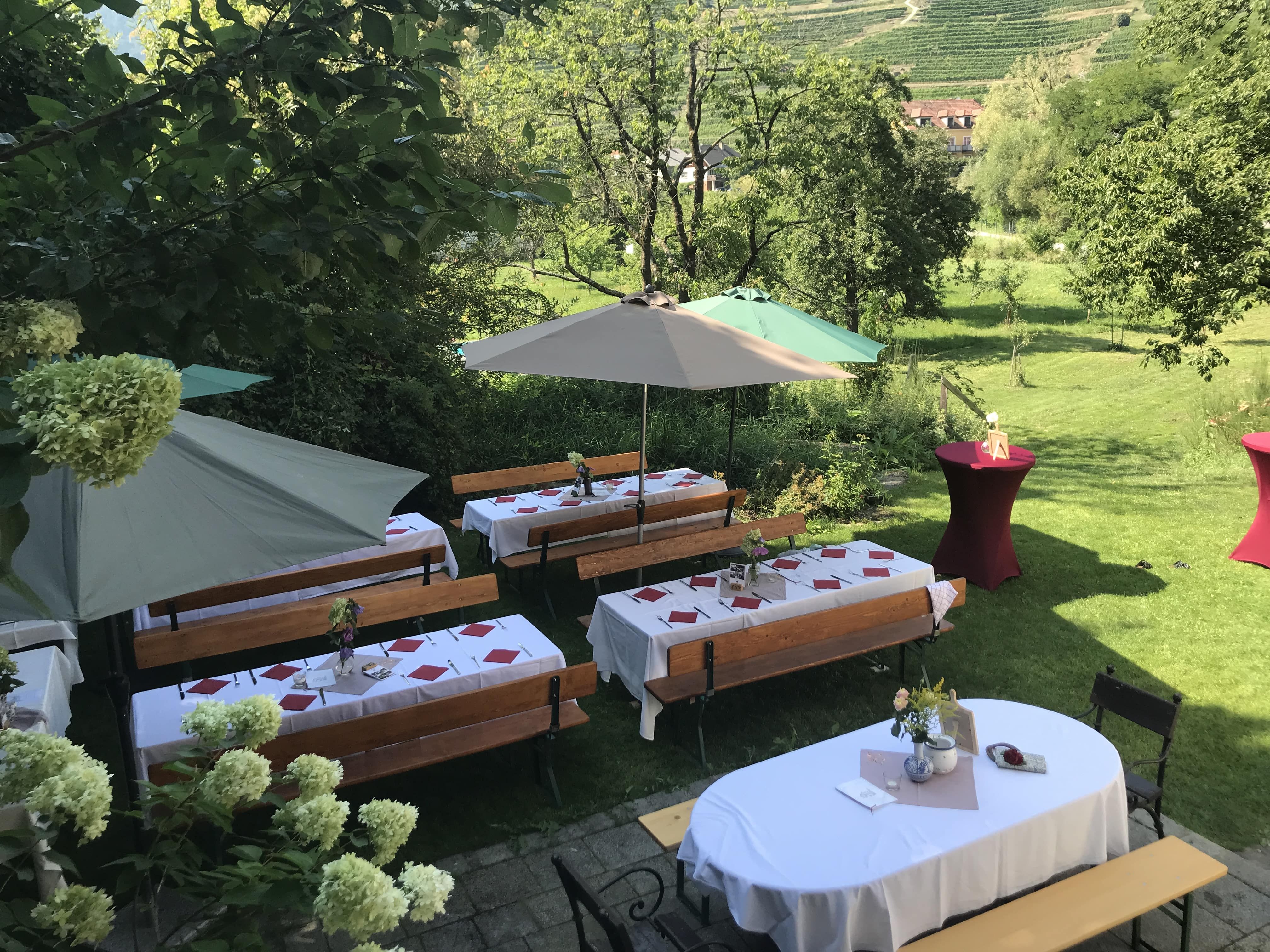 Slávnostne prestreté vonkajšie stoly so slnečníkmi a kvetinovou výzdobou.