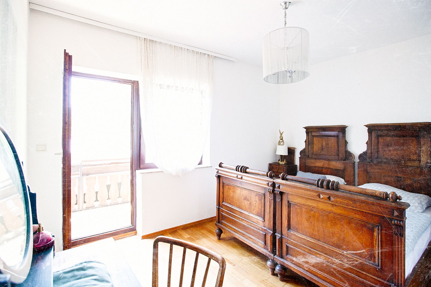 Svetlá spálňa so starožitným dreveným nábytkom a vstupom na balkón.