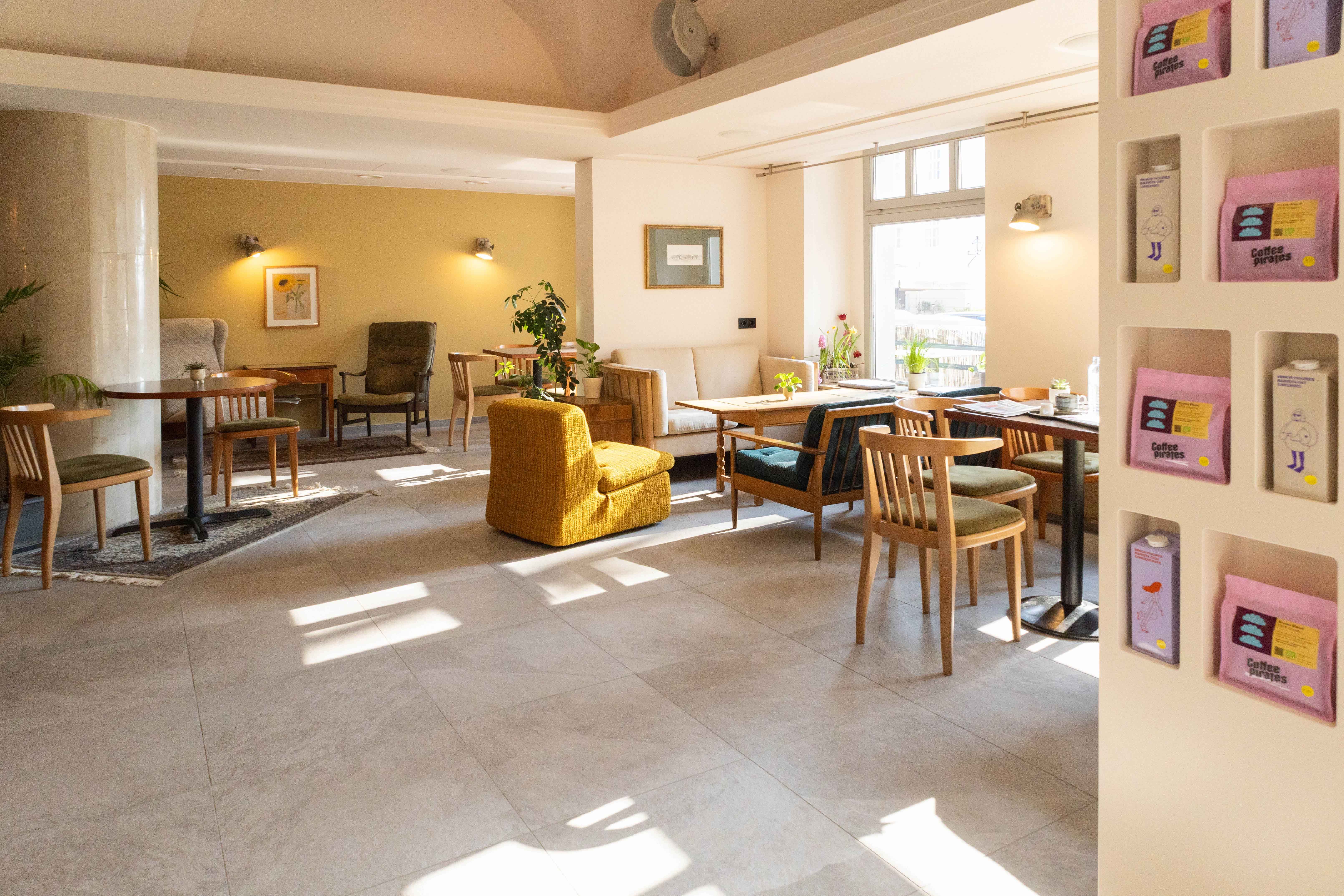 Pohľad do interiéru útulnej kaviarne s dreveným nábytkom a rastlinami.