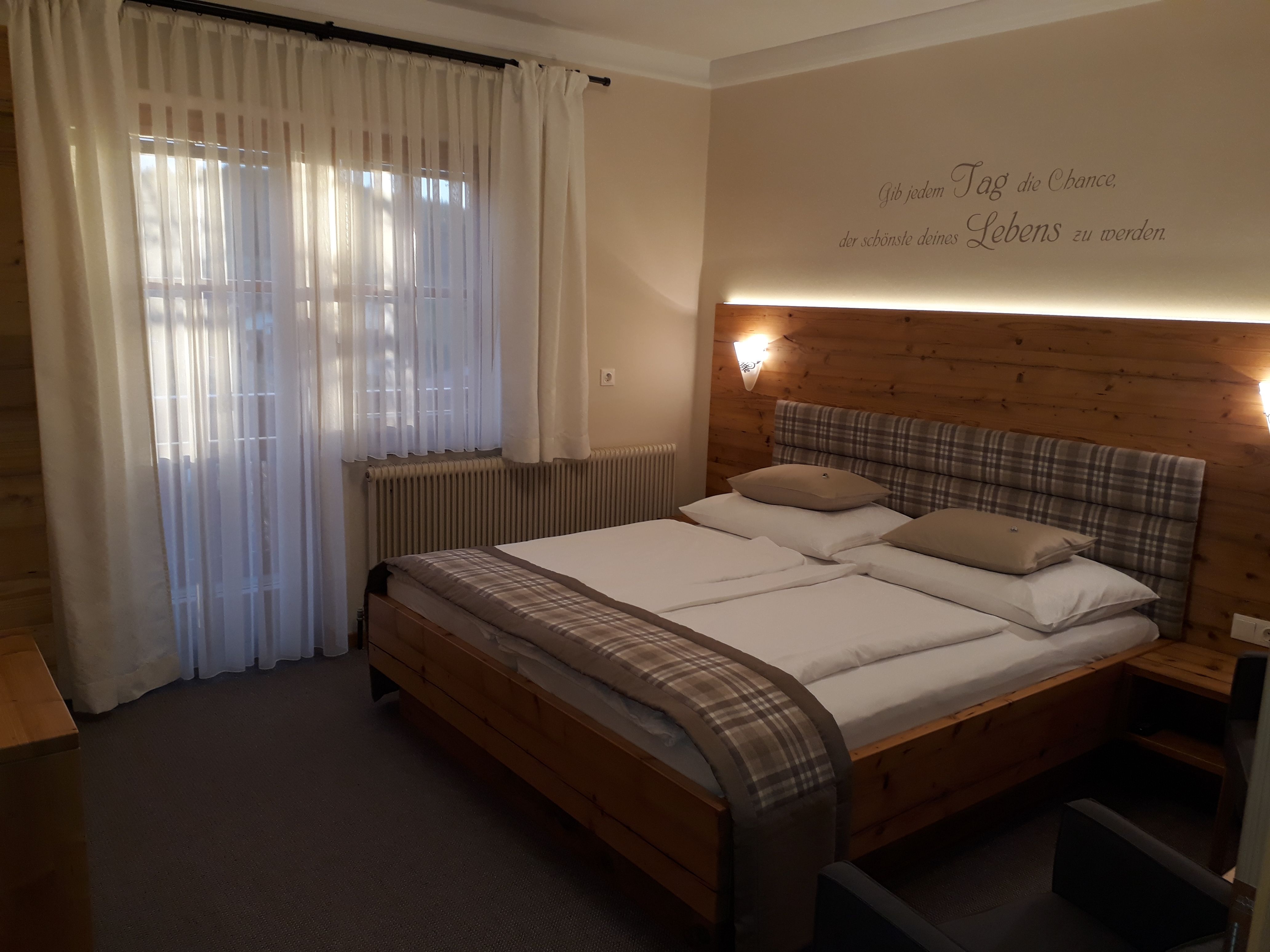 Útulná spálňa s manželskou posteľou, drevenou stenou a závesmi.