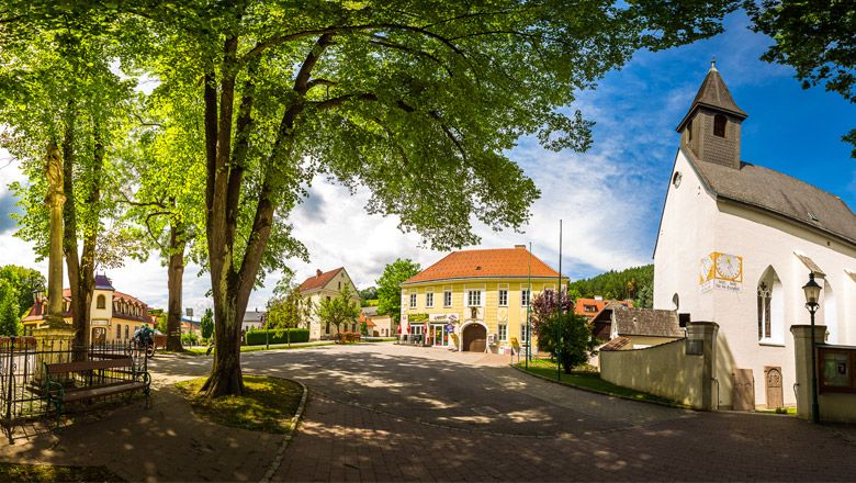 Panoramatický pohľad na námestie s kostolom, stromami a historickými budovami vo Feistritzi.