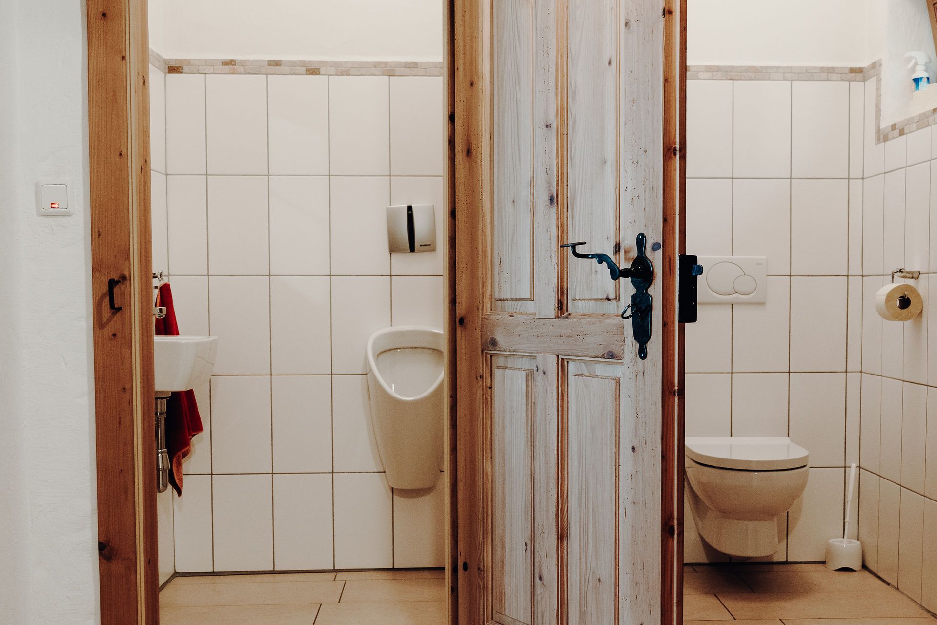 Dve toalety s drevenými dverami, pisoár a umývadlo vľavo, toaleta vpravo.