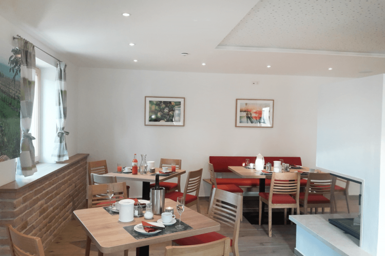 Útulná raňajková miestnosť s drevenými stolmi, červenými čalúnenými lavicami a ozdobnými obrázkami na stene.