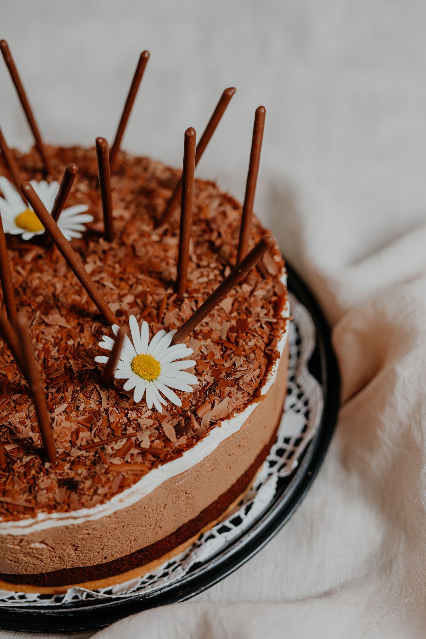 Čokoládová torta zdobená čokoládovými tyčinkami a sedmokráskami.
