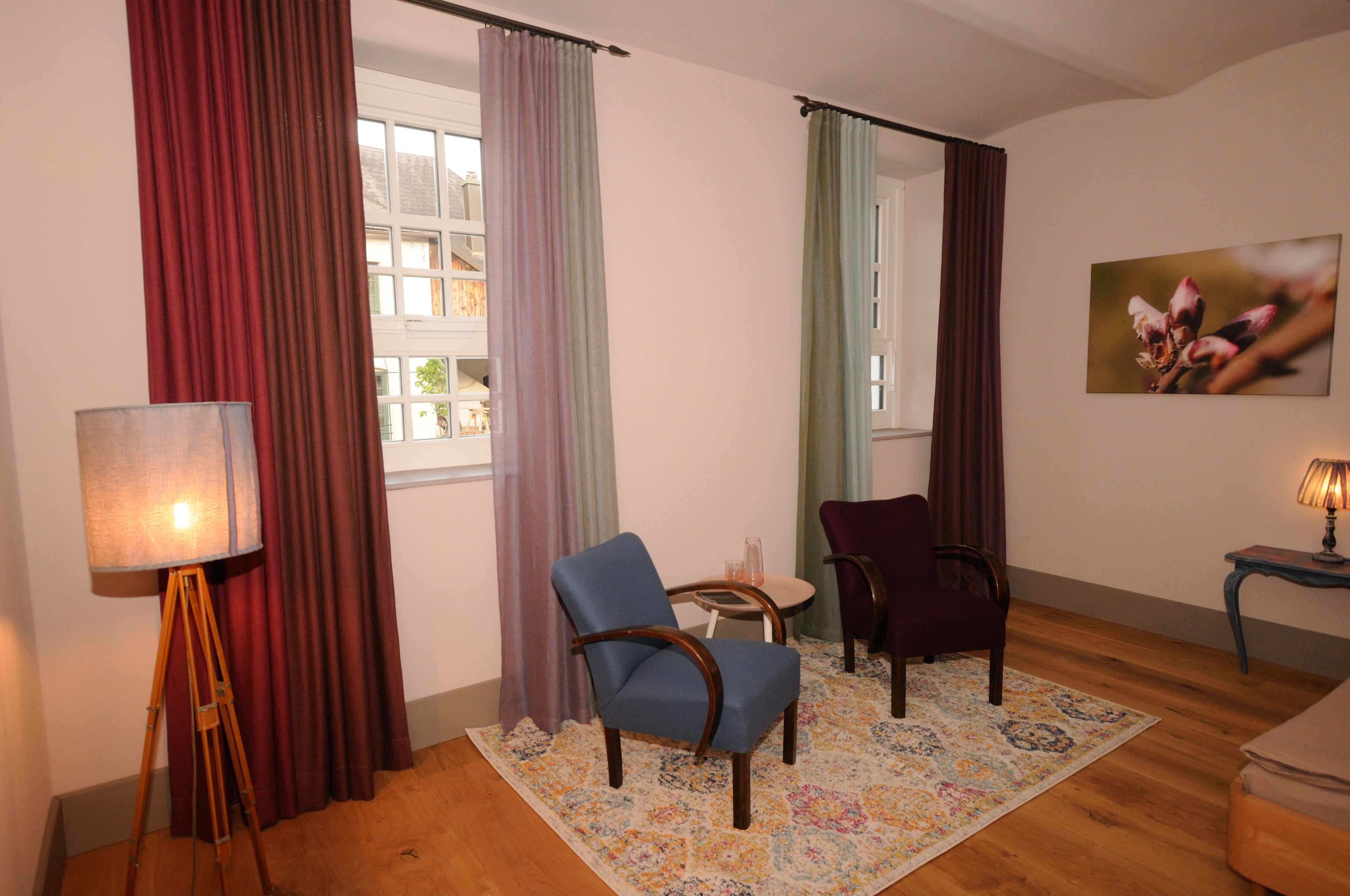 Útulná izba s dvoma kreslami, farebnými závesmi a kobercom.