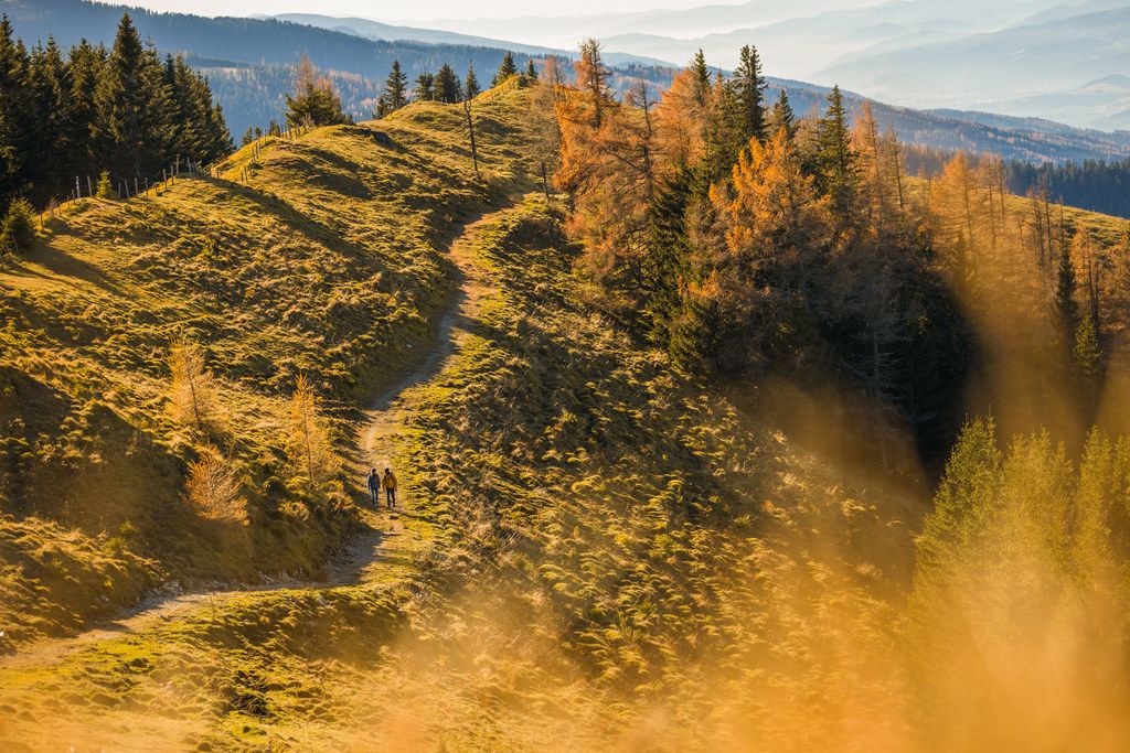 Dvaja turisti na jesennej horskej ceste s farebnými stromami.