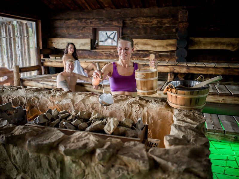 Osoba leje vodu na horúce kamene v saune.